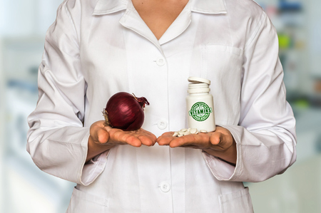 Young doctor holding fresh onion and bottle of pills with vitamins and compare themの写真素材