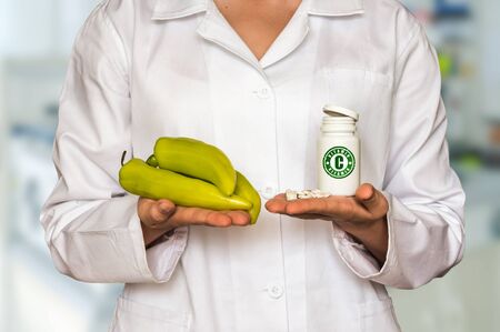 Young doctor holding fresh pepper and bottle of pills with vitamin C and compare themの写真素材
