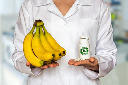 Young doctor holding fresh yellow bananas and bottle of pills with vitamin B6 and compare themの写真素材