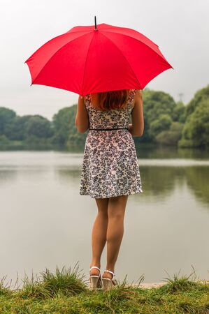 Beautiful girl with red umbrella near the pondの写真素材