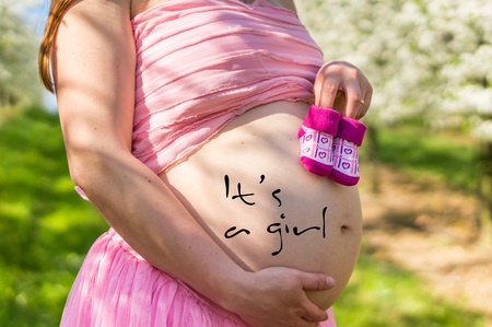 Belly of a pregnant girl and small booties in the blooming fruit gardenの写真素材