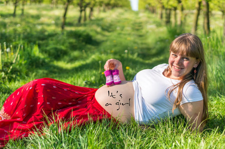 Pregnant young girl lying on the grass in the fruit garden