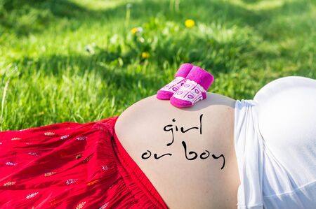 Pregnant young girl on the grass in the garden with inscription: girl or boy on her bellyの写真素材
