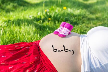 Pregnant young girl on the grass in the garden with inscription: baby on her bellyの写真素材