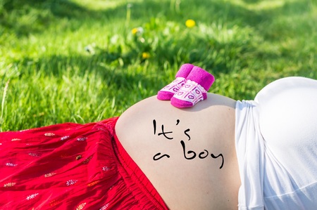 Pregnant young girl on the grass in the garden with inscription: It's a boy on her bellyの写真素材