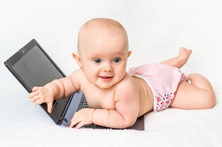 Cute baby girl in a diaper playing with laptop isolated on white blanketの写真素材