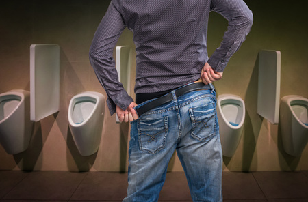Standing man peeing to a urinal in restroom or incontinence conceptの写真素材