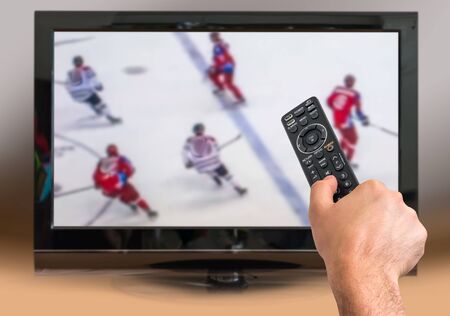 Man is watching hockey match on TV and holds remote controller in handの写真素材