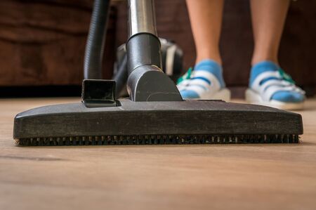 Woman with vacuum cleaner cleaning wooden laminate floor at homeの写真素材