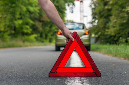 Driver putting out a traffic warning sign - broken car on the roadの写真素材