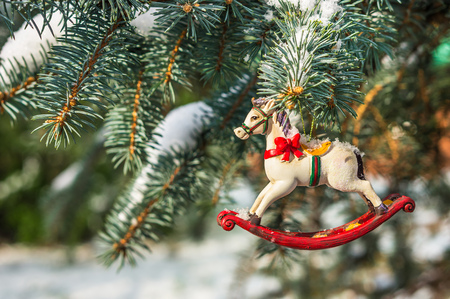 Rocking horse, closeup of Christmas tree decoration on snowy pine branchの写真素材