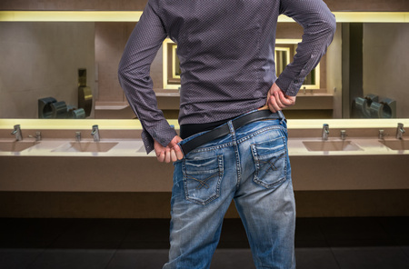 Man adjusts after peeing on the public toilet in restroomの写真素材