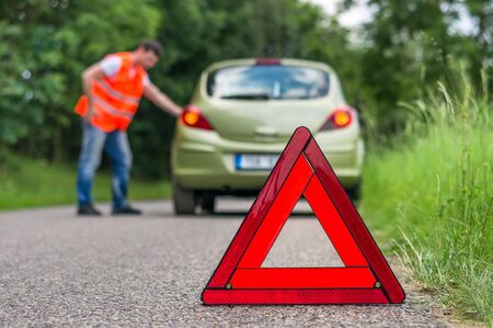 Broken car on the road and unhappy driver with red warning triangleの写真素材