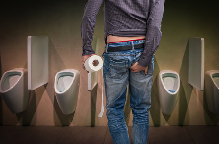 Man holding toilet paper roll and holding his butt in restroom. Diarrhea concept.の写真素材