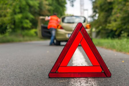 Driver pushes broken car and red warning triangle - broken car on the roadの写真素材