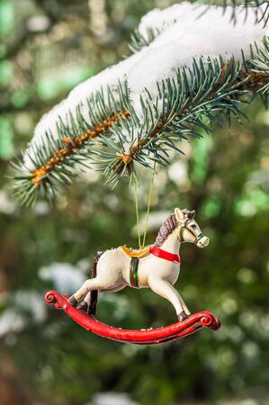 Rocking horse, closeup of Christmas tree decoration on snowy pine branchの写真素材