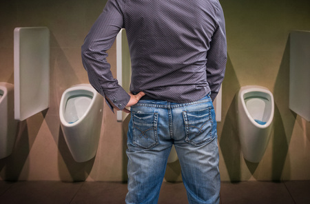 Standing man peeing to a urinal in restroom or incontinence conceptの写真素材