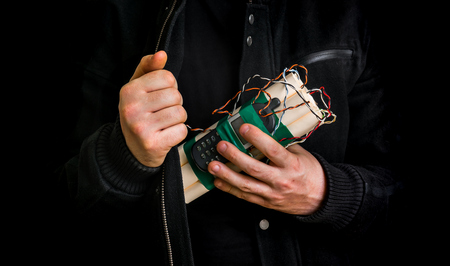 Dangerous terrorist in black jacket with dynamite bomb in hand isolated on black backgroundの写真素材