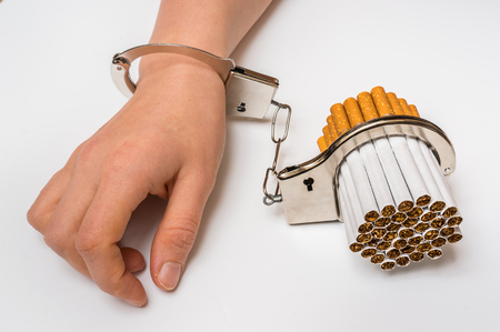 Female hand with handcuffs and cigarettes on white background - concept of smoking dependenceの写真素材
