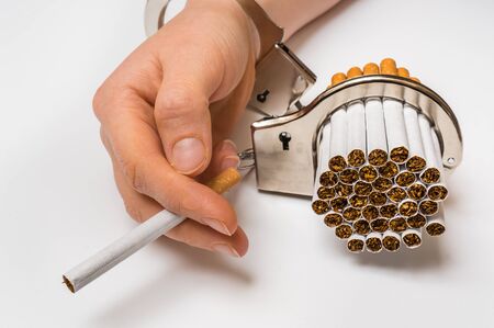 Female hand with handcuffs and cigarettes on white background - concept of smoking dependenceの写真素材