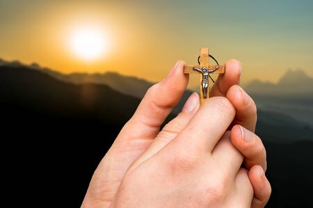 Female hands with wooden cross and sunset in the mountains - religion conceptの写真素材