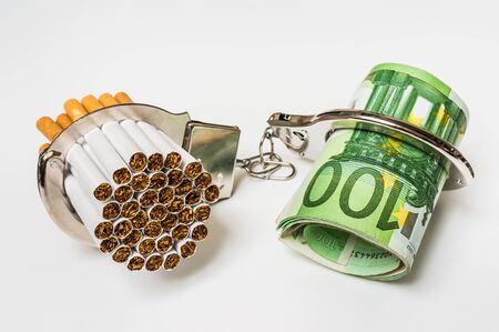 Cigarettes and money with handcuffs as a concept of smoking costの写真素材