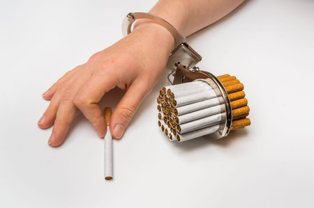 Female hand with handcuffs and cigarettes on white background - concept of smoking dependenceの写真素材