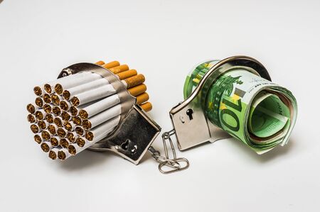 Cigarettes and money with handcuffs as a concept of smoking costの写真素材