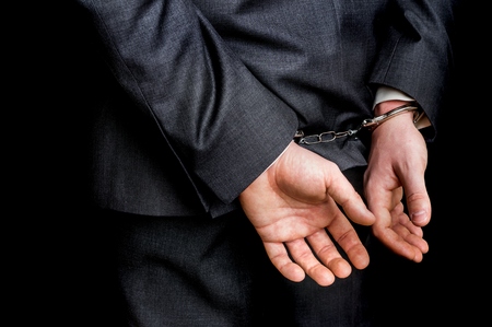 Arrested businessman in handcuffs with hands behind back - isolated on black backgroundの写真素材