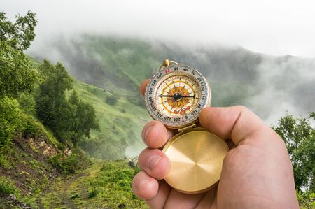 Traveler man with compass seeking a right way through the fog in mountains - navigation conceptの写真素材