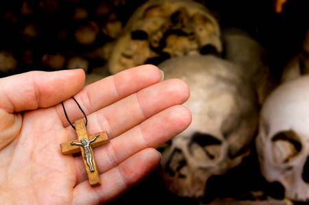 Female hand with wooden cross on skulls and bones background - religion conceptの写真素材
