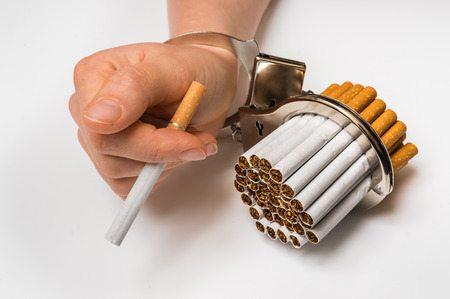 Female hand with handcuffs and cigarettes on white background - concept of smoking dependenceの写真素材