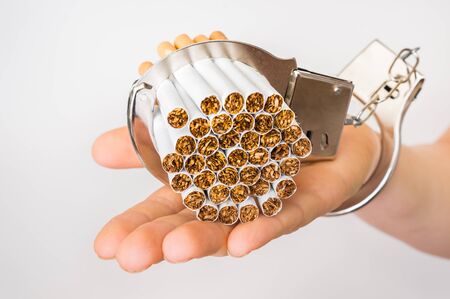 Female hand with handcuffs and cigarettes on white background - concept of smoking dependenceの写真素材