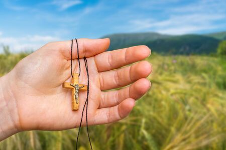 Female hand with wooden cross on rye field background - religion conceptの写真素材