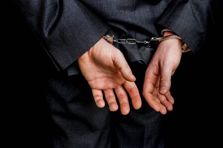 Arrested businessman in handcuffs with hands behind back - isolated on black backgroundの写真素材