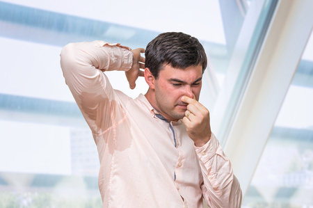 Business man with sweating under armpit pinches nose with fingers in officeの写真素材
