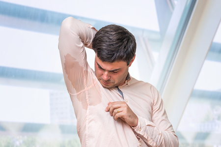 Man with hyperhidrosis sweating under armpit in pink shirtの写真素材