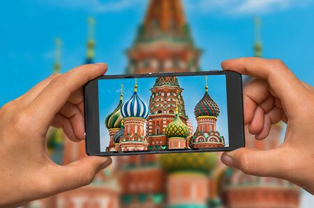 Woman hands with mobile cell phone to take a photo of St. Basils cathedral and monument to Minin and Pozharsky on Red Square in Moscow, Russiaの写真素材
