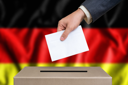 Election in Germany. The hand of man putting his vote in the ballot box. German flag on background.の写真素材