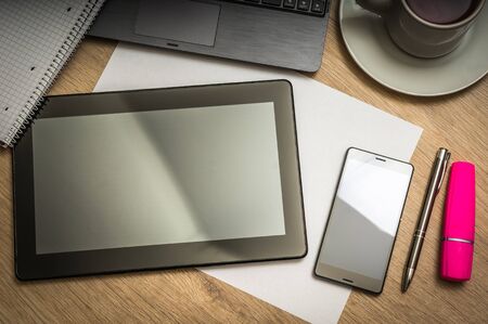 Workplace with digital tablet, mobile phone, paper, pen, laptop and cup of coffee on wooden table - above viewの写真素材
