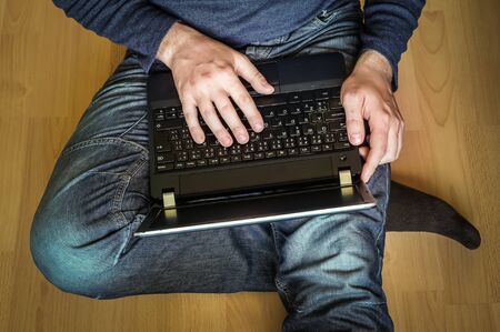 Young student using laptop and sitting on the wooden floor in classroomの写真素材