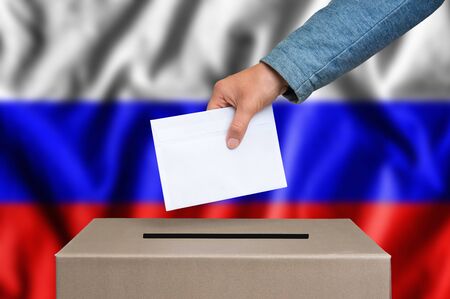 Election in Russia. The hand of woman putting her vote in the ballot box. Russian flag on background.の写真素材