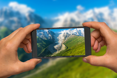 Woman hands with mobile cell phone to take a photo of snow mountains and glacier in Georgiaの写真素材