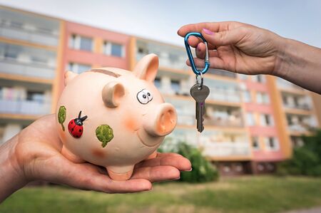 Real estate agent giving flat keys to a new property owner, who is paying last saving money from piggy bank on blurred backgroundの写真素材