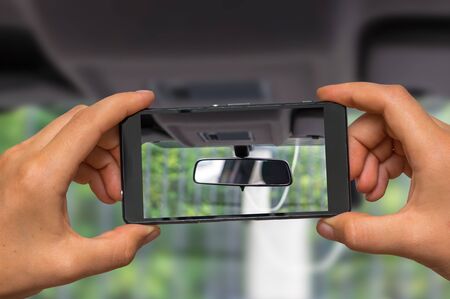 Woman hands with mobile cell phone to take a photo of car rearview mirrorの写真素材