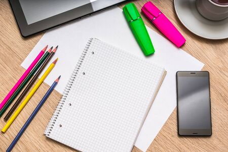 Workplace with blank white notepad, mobile phone, paper, pencils, tablet and cup of coffee on wooden table - above viewの写真素材