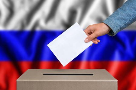 Election in Russia. The hand of woman putting her vote in the ballot box. Russian flag on background.の写真素材