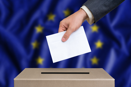 Election in European Union. The hand of man putting his vote in the ballot box.  European Union flag on background.の写真素材
