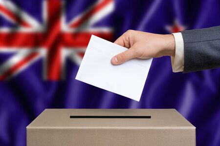 Election in New Zeland. The hand of man putting his vote in the ballot box. New Zeland flag on background.の写真素材