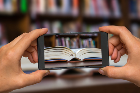 Woman hands with mobile cell phone to take a photo of open book on the table in libraryの写真素材